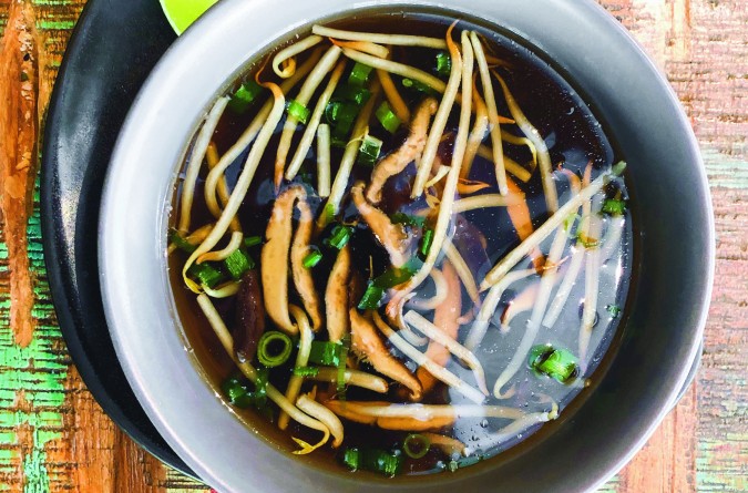 Clear vegetable soup with sprouts and mushrooms on a colorful table